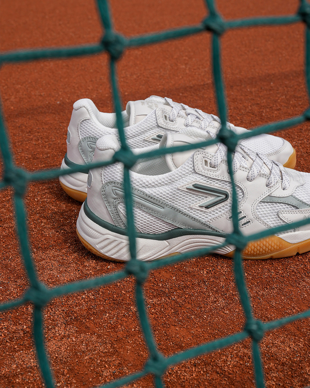 The ACE Hub ACE 25 sneaker in off-white cucumber, photographed on clay court behind net

