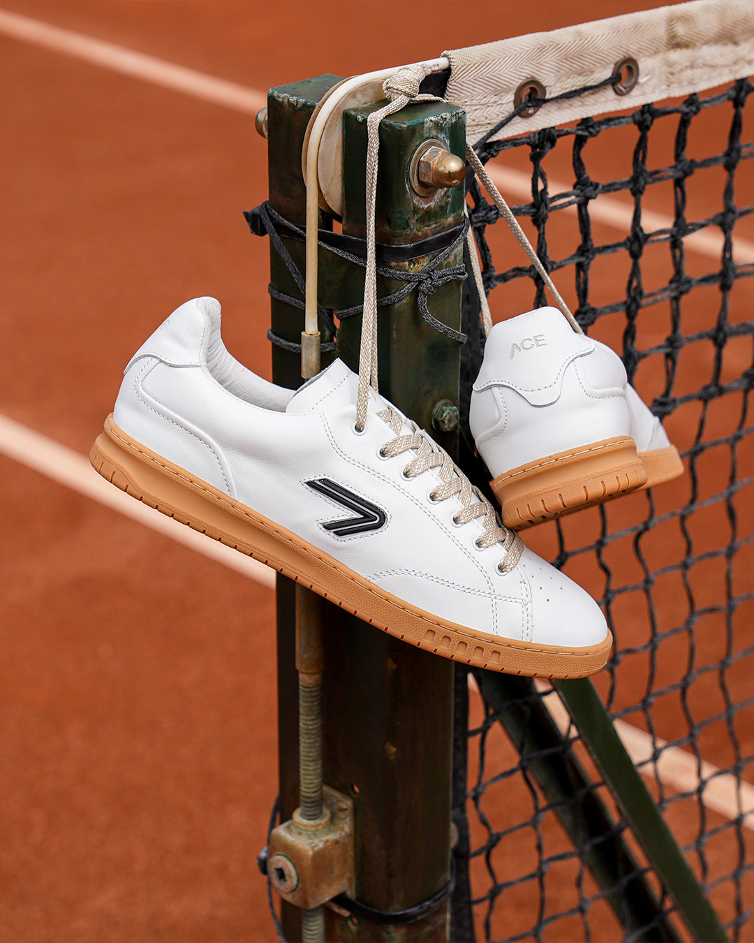 The ACE Hub Shot sneakers in white with gum sole, hanging on tennis net

