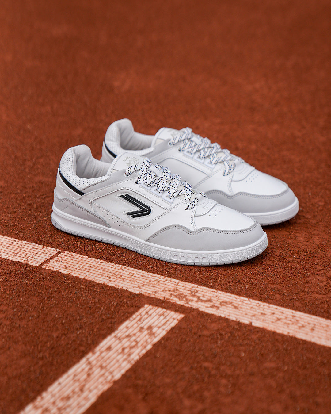 The ACE Hub Sprint sneakers in white and black, photographed on clay court at De Mets The Hague

